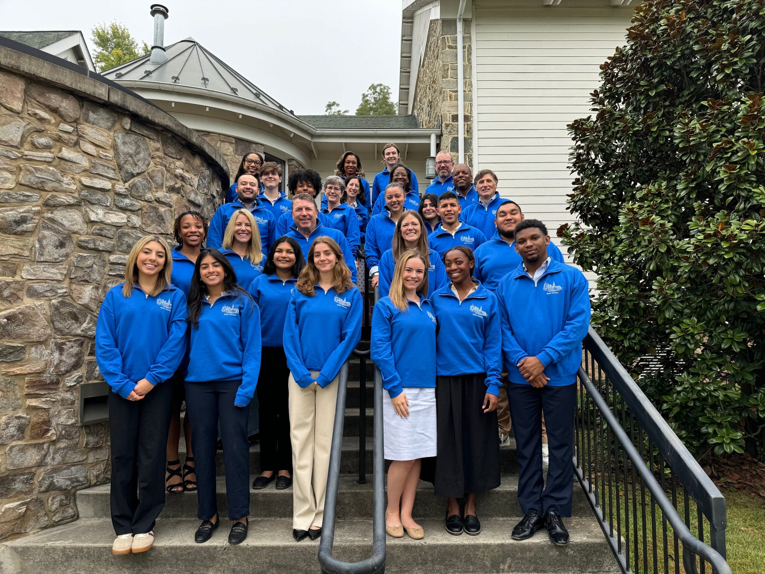 Baker Scholars and Trustees gathered on the steps in blue quarterzips smiling for a photo. 